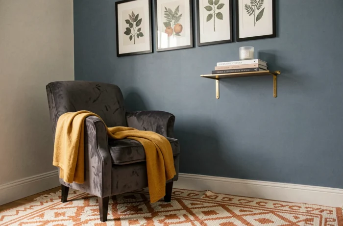 Coin lecture cosy avec fauteuil en velours anthracite, mur bleu profond et galerie de cadres botaniques dans une chambre décorée